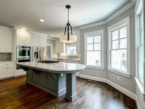 Bright modern kitchen with large marble island, white cabinets, stainless steel appliances, hardwood floors, and large windows