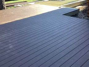 View of a newly constructed dark wood deck and an unfinished section under construction with a handyman service van nearby.