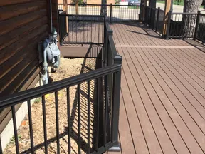 Spacious brown wooden deck with black metal railings next to a log cabin and trees in the background.