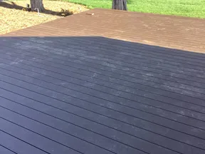 Two-tone wooden deck patio with black and brown planks under daylight near road and trees.