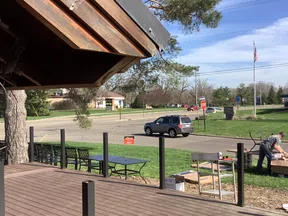 Outdoor deck under construction near a road with a man working and a parked SUV on a sunny day.