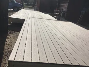 Newly constructed brown wooden deck extending from a house under a partly cloudy sky.