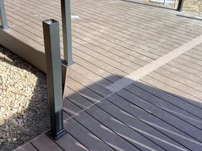 Newly constructed brown composite wood deck with metal posts for railing under sunlight in outdoor setting.