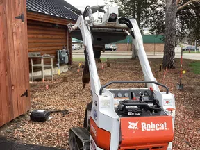 Compact Bobcat MT55 mini track loader parked near a wooden cabin on a construction site.