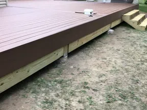 Newly built brown wooden backyard deck with stairs next to house and garden shed on grassy ground.