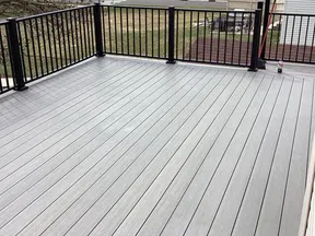 Spacious outdoor deck with gray composite wood flooring and black metal railing overlooking a backyard.