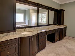 Spacious bathroom vanity with dark wood cabinets, granite countertop, dual sinks, and large framed mirror.
