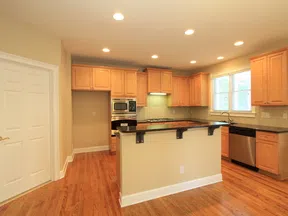 Bright modern kitchen with wooden cabinets, black countertops, stainless steel appliances, and hardwood floors.
