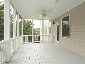 Bright spacious screened porch with white railing, ceiling fan, beige siding, and natural outdoor view.