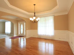 Empty dining room with hardwood floors, beige walls, white wainscoting, chandelier, and a window with sheer curtains