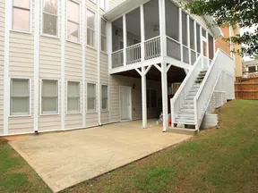 House exterior with beige siding, concrete patio, white screened porch, and stairs leading to backyard.