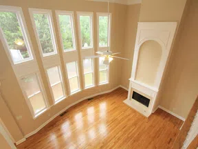Bright spacious living room with tall windows, hardwood floors, and a white fireplace under high ceilings.