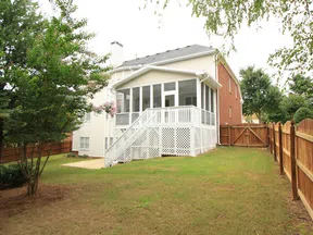 Backyard view of a house with a white screened porch and wooden fence surrounding the grassy yard.