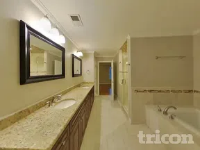 Spacious bathroom with double sink granite countertop, large mirrors, bathtub, and glass shower enclosure.