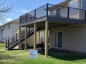New elevated wooden deck with black metal railings attached to beige house with advertisement sign on green lawn.