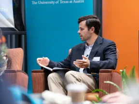 Man in blazer and khakis speaking while seated in armchair at University of Texas event panel discussion