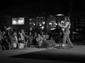 Black and white image of a female singer playing guitar on stage with an attentive crowd watching at night.
