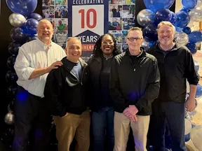 Group of five people smiling in front of a 10 years anniversary celebration banner with blue and silver balloons.