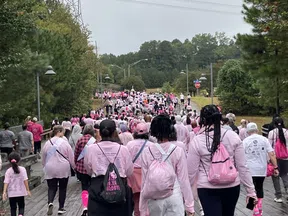Crowd of people walking outdoors wearing pink clothing for a breast cancer awareness event on a wooden path.