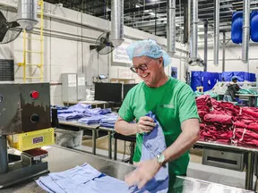 Smiling factory worker in green shirt sorting blue and red garments inside a large industrial facility.