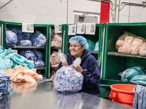 Worker in hairnet packing fabric bundles in a textile factory with shelves of sorted materials behind.