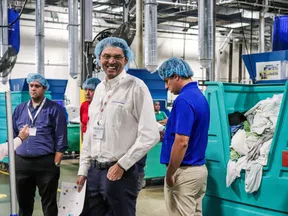 Workers wearing hairnets and badges inside a busy industrial laundry facility with large bins of linens.