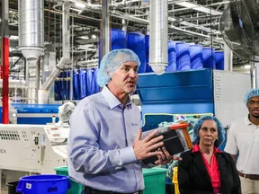 Man in hairnet speaking in factory environment with machinery and two colleagues listening attentively.
