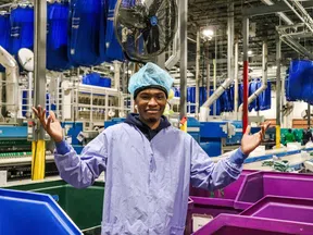 Worker in protective clothing standing in a busy industrial laundry facility with sorting bins and machinery.