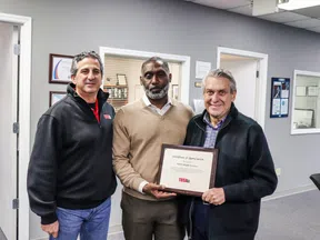 Three men standing in an office holding a framed certificate of appreciation from TRSA.