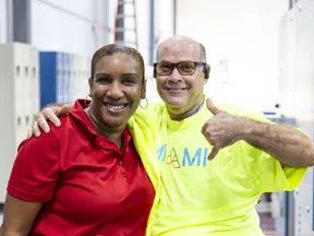 Two factory workers smiling together, one in red shirt and the other in yellow, showing a thumbs-up gesture indoors.