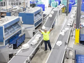 Industrial laundry facility with conveyor belts sorting folded white linens and a worker in a neon yellow shirt raising arms.