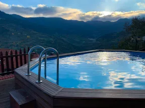 Outdoor above-ground pool with metal ladder overlooking mountains at sunset under cloudy sky.
