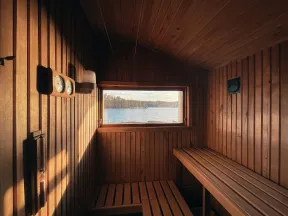 Wood-paneled sauna interior with benches and a window showing a lake and forest view in natural light