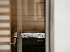 Sauna interior with wooden bucket and bench covered by a gray towel beside wooden panel walls.