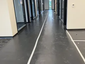 Long office hallway with black polished floor, white lines, glass doors, and footprints on the floor.