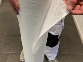 Person holding and peeling off a sheet from a large roll of white fabric or paper material indoors.
