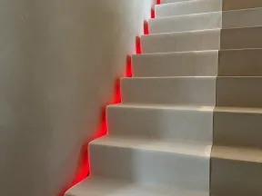 Modern staircase with beige steps illuminated by red LED lights along the left side under the handrail.