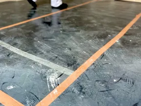 Painter walking on taped floor wearing white coveralls and black boots holding a paint roller in hand.