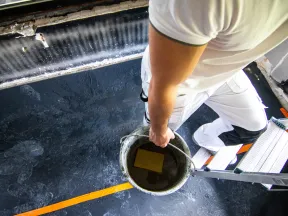 Painter in white clothes holding a bucket while standing on a ladder during interior painting work.