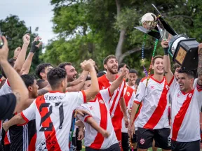 Soccer team celebrating with championship trophy, wearing white and red jerseys, cheering and lifting the cup outdoors.
