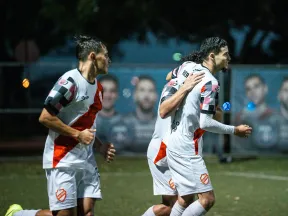 Soccer players in white and red uniforms celebrating on the field during a nighttime match.