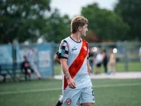 Soccer player in white and red uniform standing on a green field during a game with blurred spectators in background