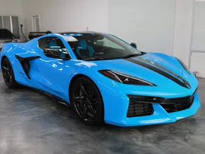 Blue sports car with black racing stripe parked indoors on polished concrete floor.