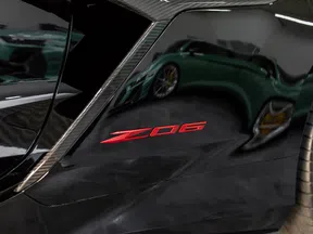 Close-up of black car panel with red Z06 emblem and carbon fiber trim near rear wheel.