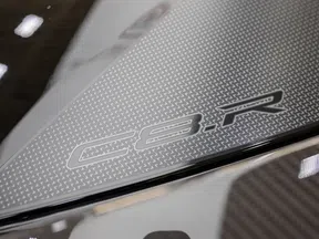 Close-up of Corvette C8.R logo on textured carbon fiber car part with reflective surfaces and lighting.