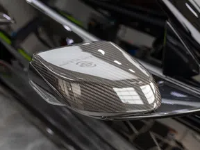 Close-up of a carbon fiber car side mirror with black glossy finish and clear turn signal light.