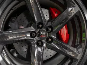 Close-up of a carbon fiber car wheel with drilled brake rotor and red brake caliper.