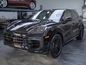 Black luxury Porsche SUV parked inside a modern garage with polished concrete floor and another car on a lift.