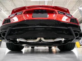 Low angle view of a red sports car rear showcasing exhaust pipes and diffuser under bright garage lighting