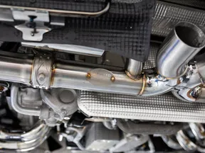 Close-up of stainless steel aftermarket car exhaust system showing pipes and welds under vehicle.